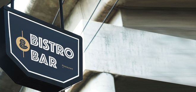 Black hanging sign reading “BISTRO BAR” on a concrete building exterior.