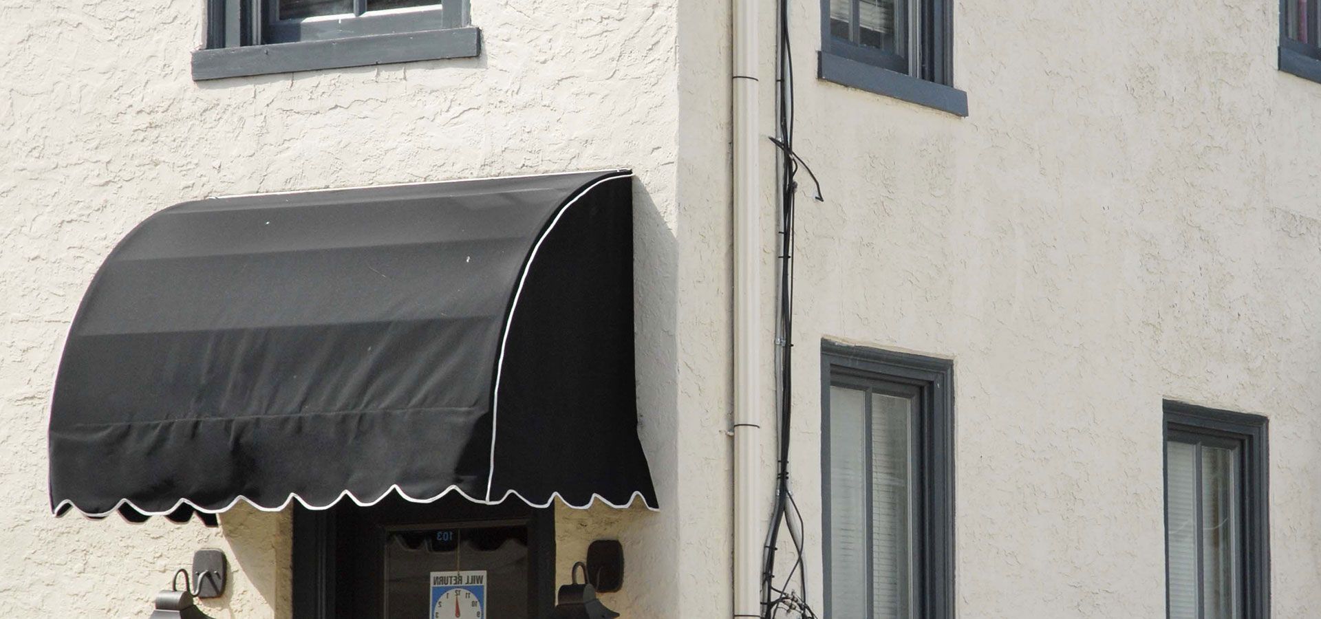Black awning over a beige building corner with gray-trimmed windows and a decorative scalloped edge