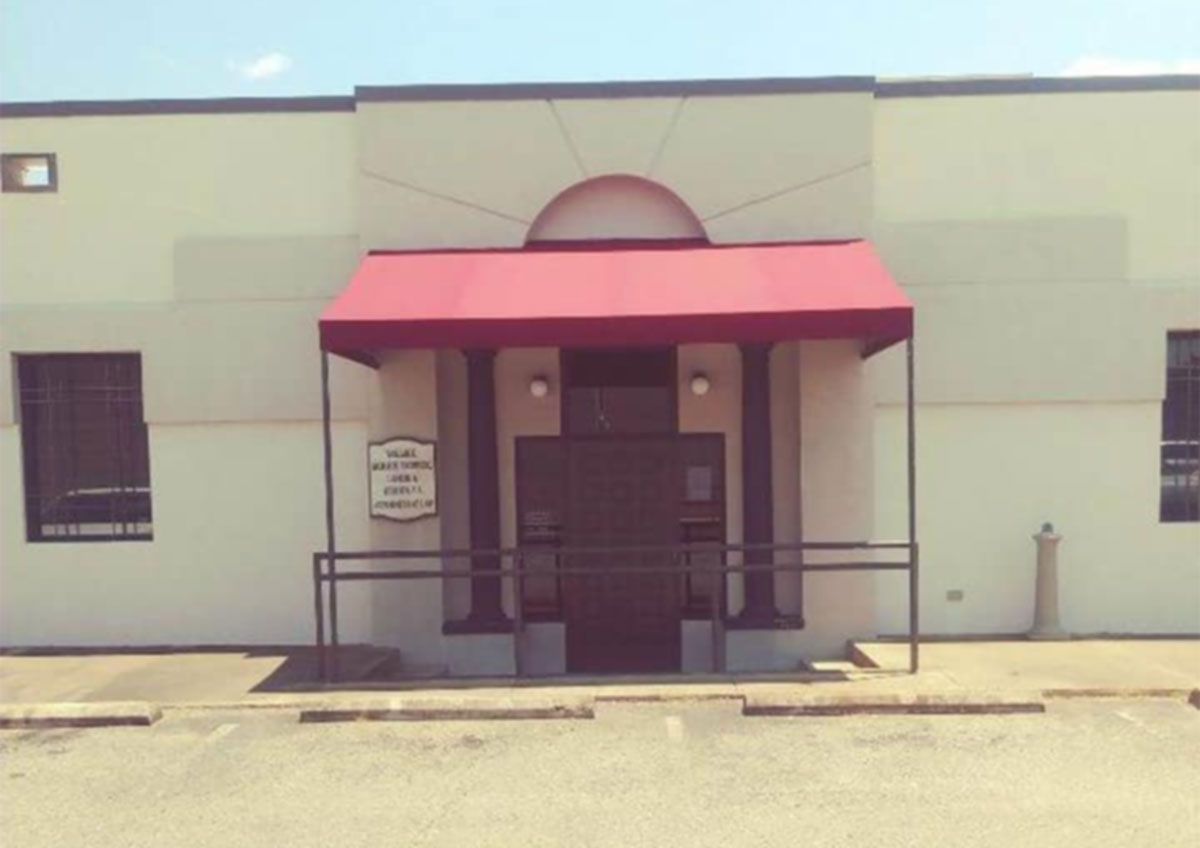 Front entrance of a building with a red awning and ramp, viewed from the street.