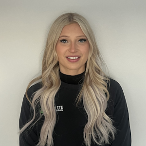 A woman with long blonde hair is wearing a black sweater and smiling.