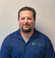 A man with a beard is wearing a blue shirt and smiling.