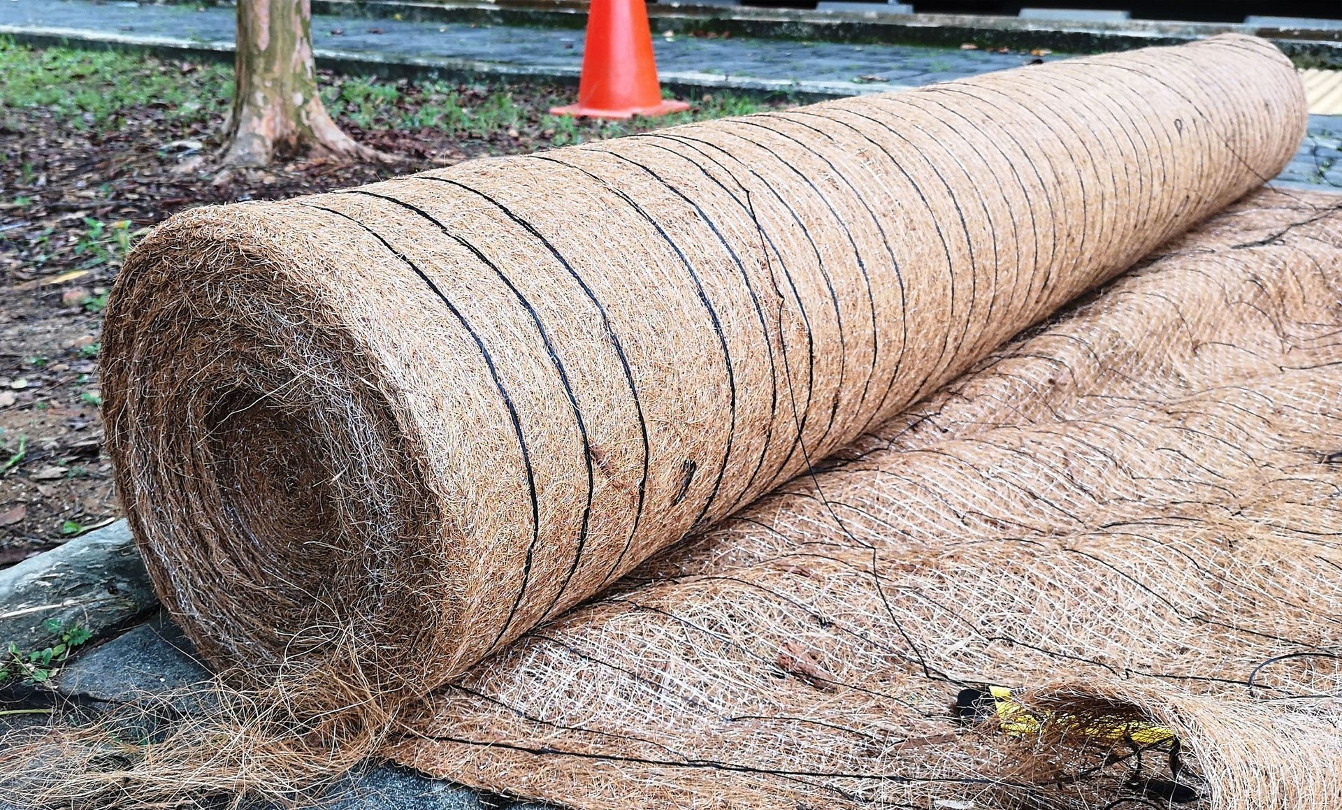 A large roll of hay is sitting on the ground next to an orange cone.