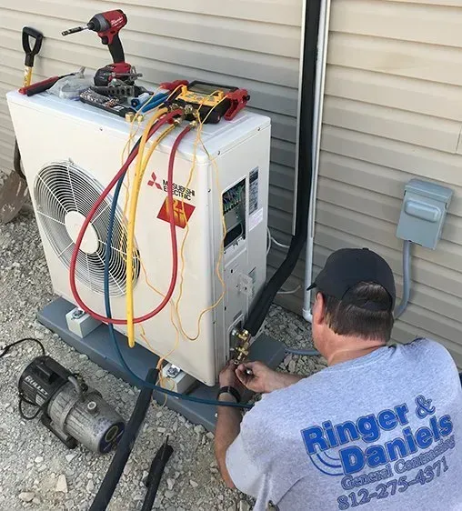 HVAC technician working on a Mitsubishi heat pump outdoors. He is connecting fittings with gauges attached.