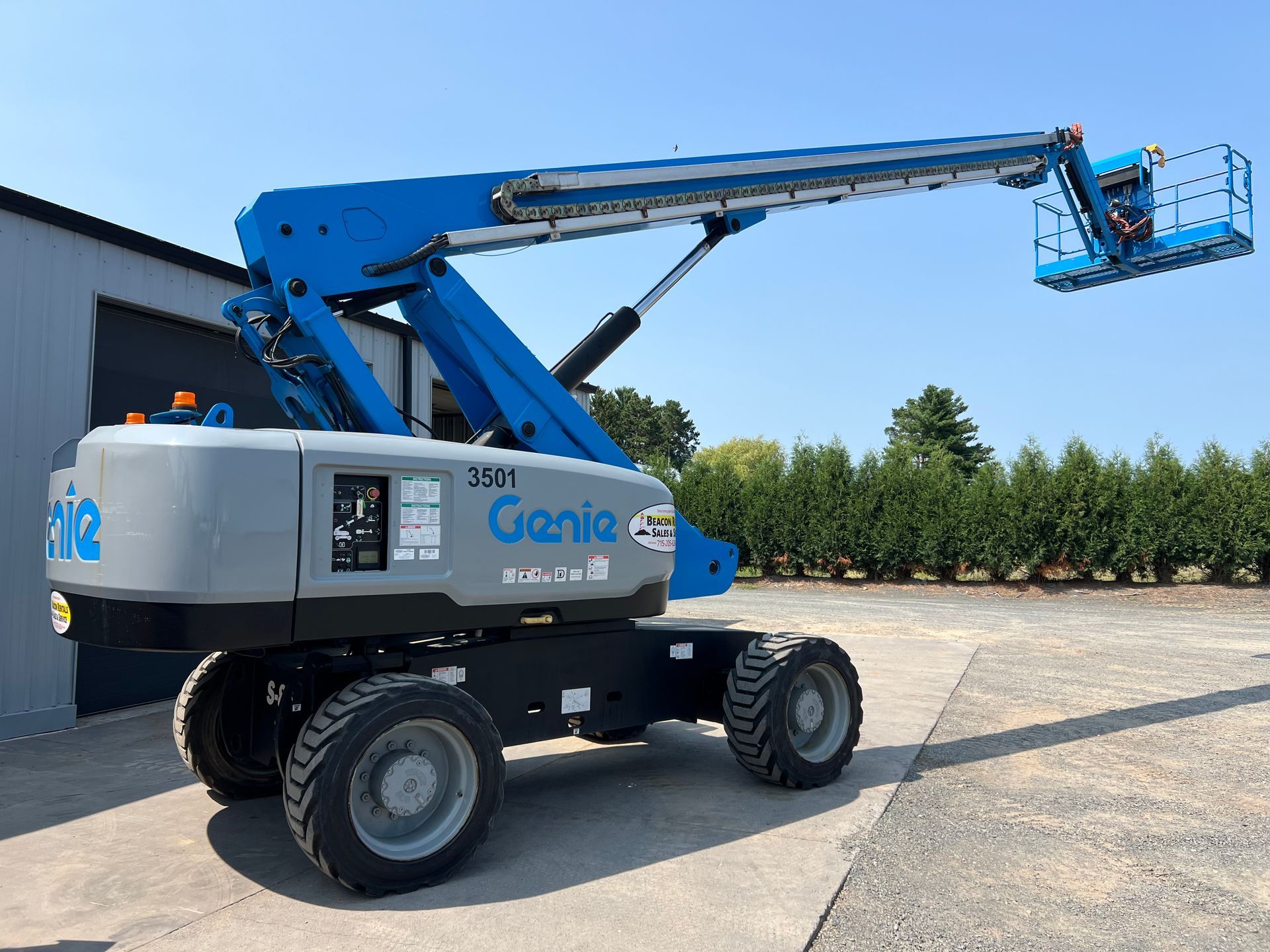 Blue Genie boom lift extended outdoors on a sunny lot next to a warehouse.