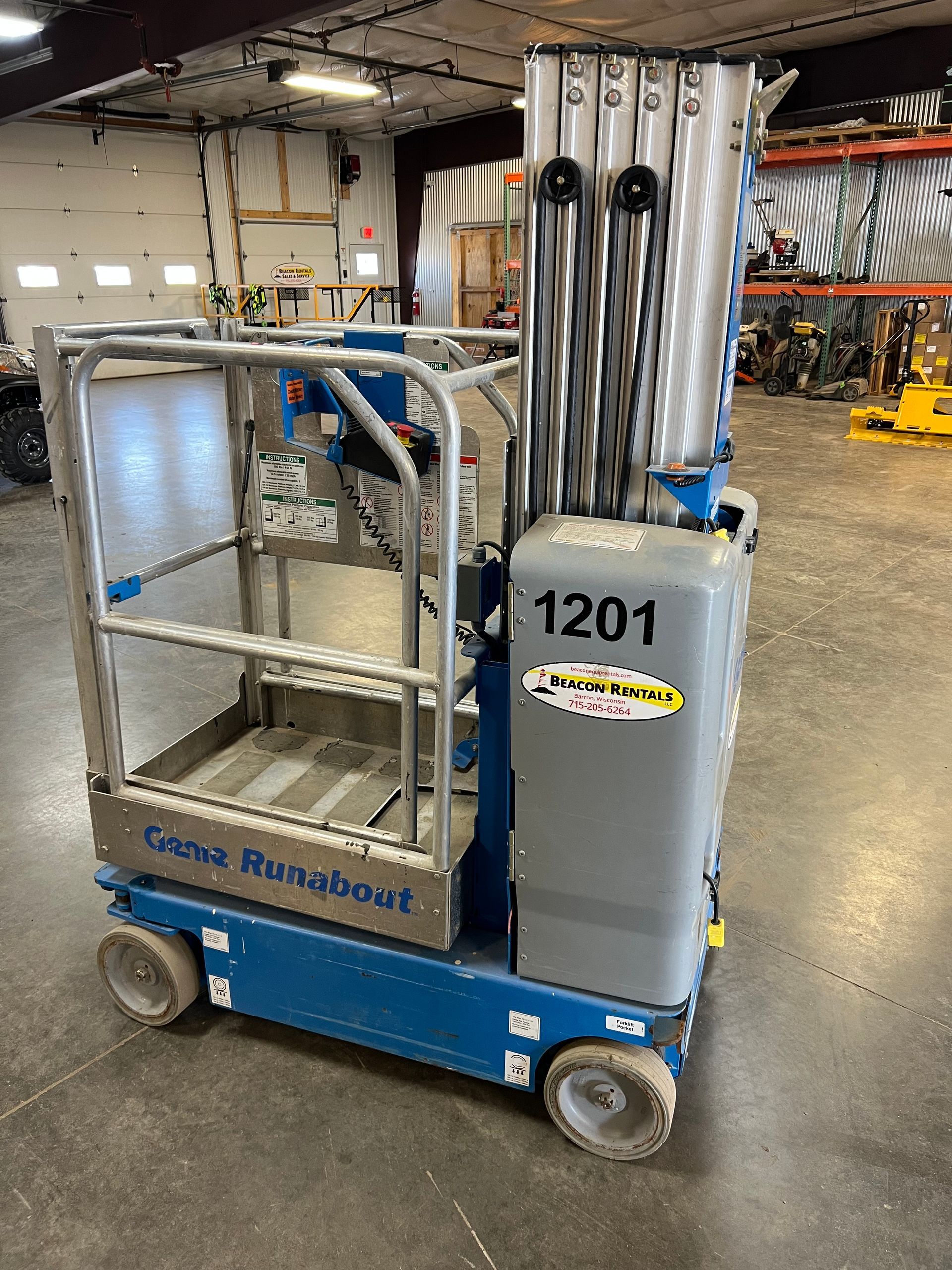 Blue industrial lift cart with metal railings and upright tubes in a warehouse.