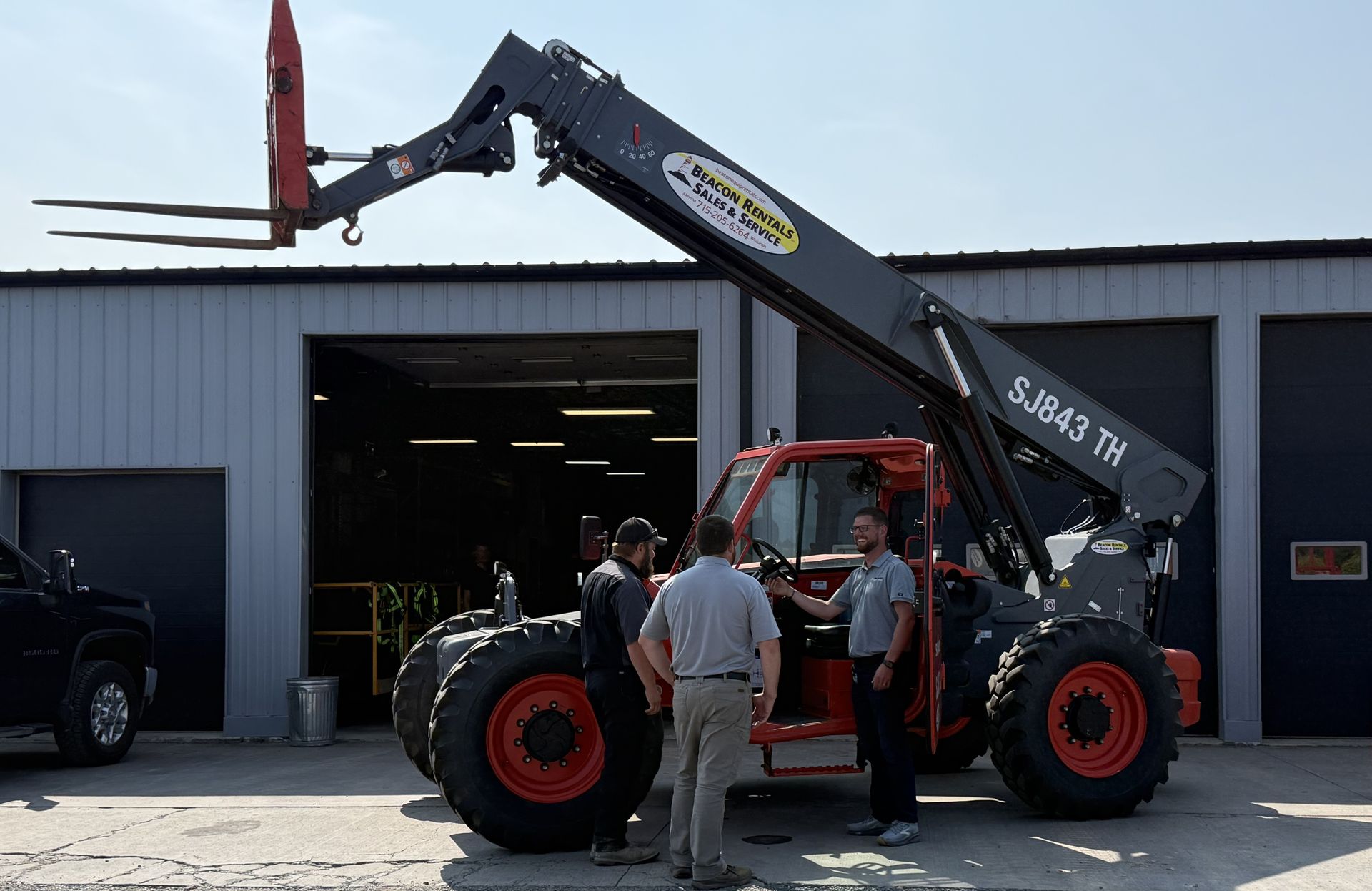 Telehandler lifting a forklift fork attachment outside a warehouse.