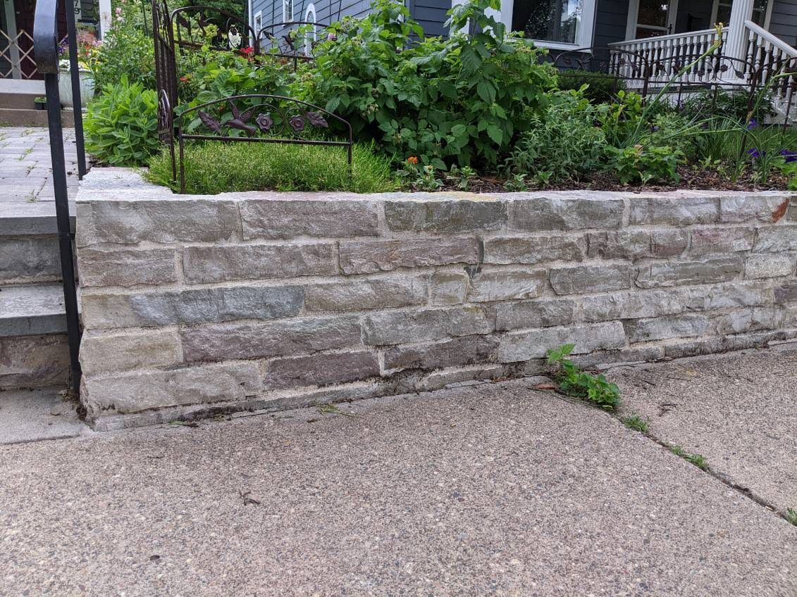 A stone wall is sitting on the sidewalk in front of a house.
