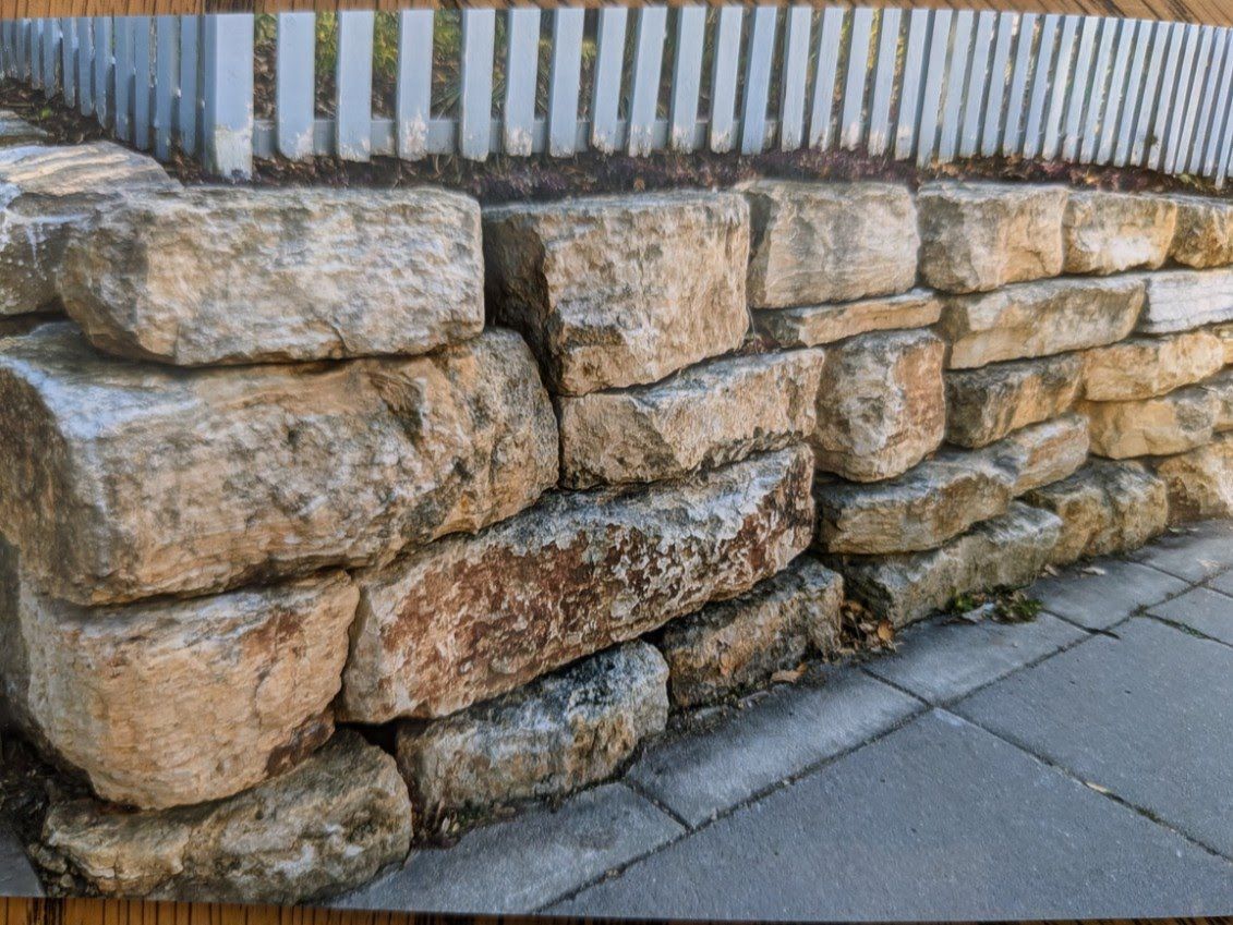 A stone wall with a wooden fence in the background