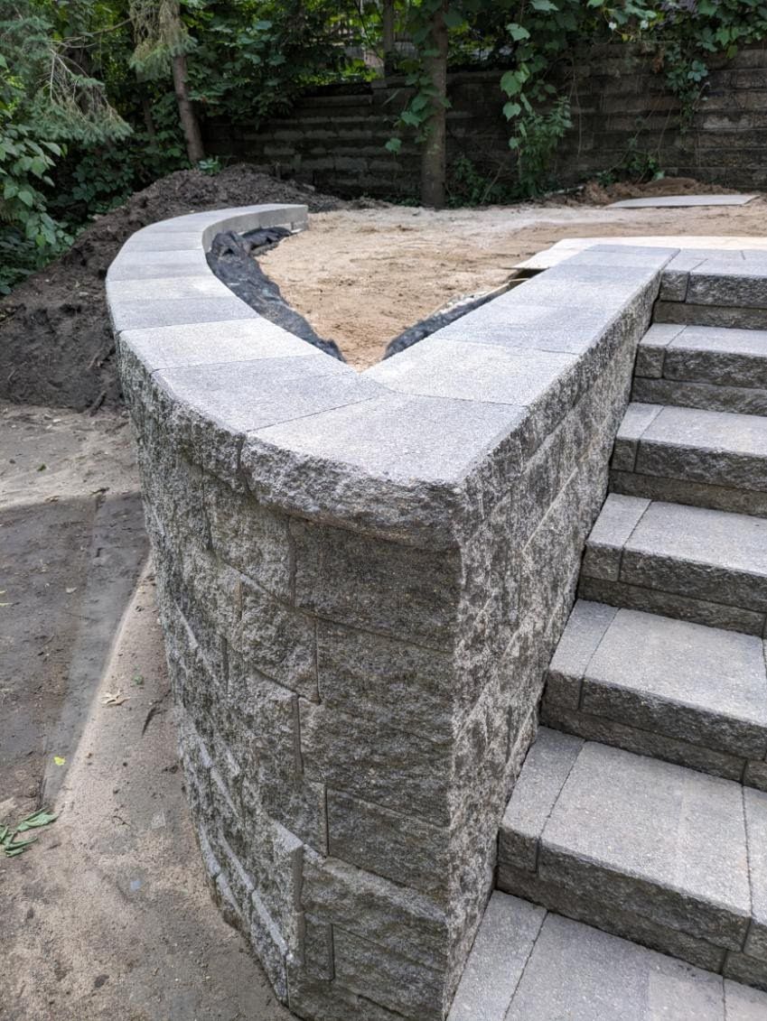 A stone wall and stairs are being built in a backyard.
