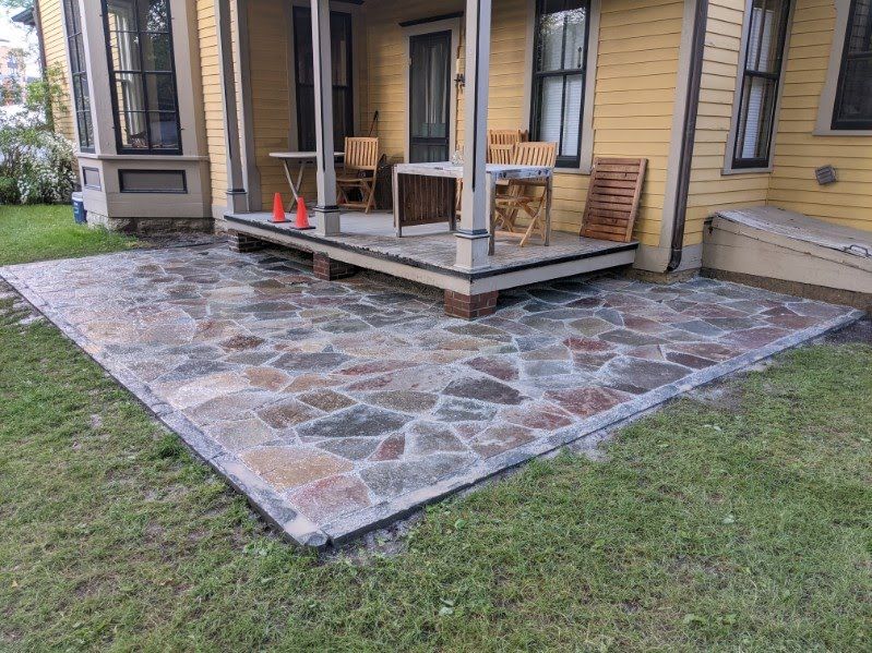 A yellow house with a stone patio in front of it.