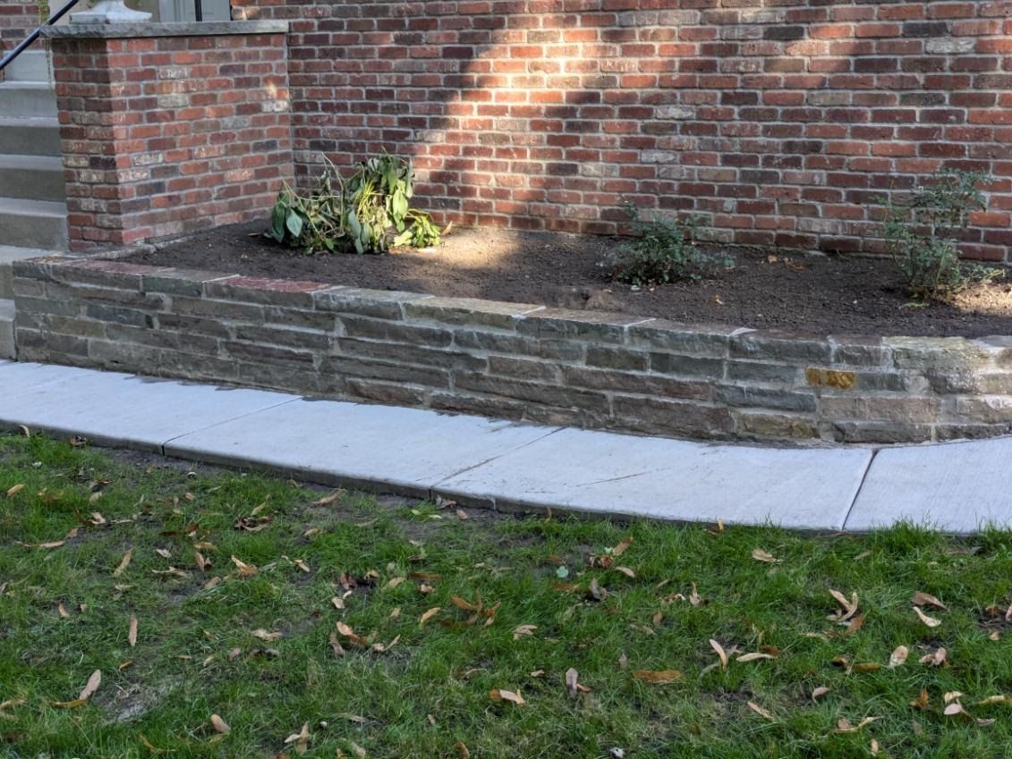 A brick wall with a planter and a sidewalk in front of it.
