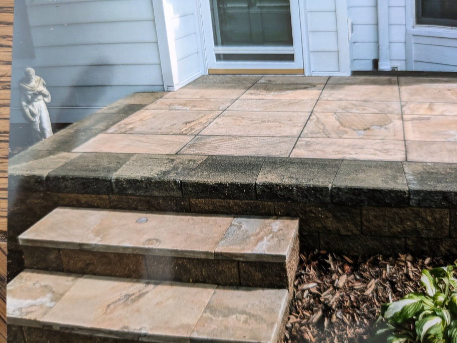 A patio with stairs leading up to it and a white house in the background.