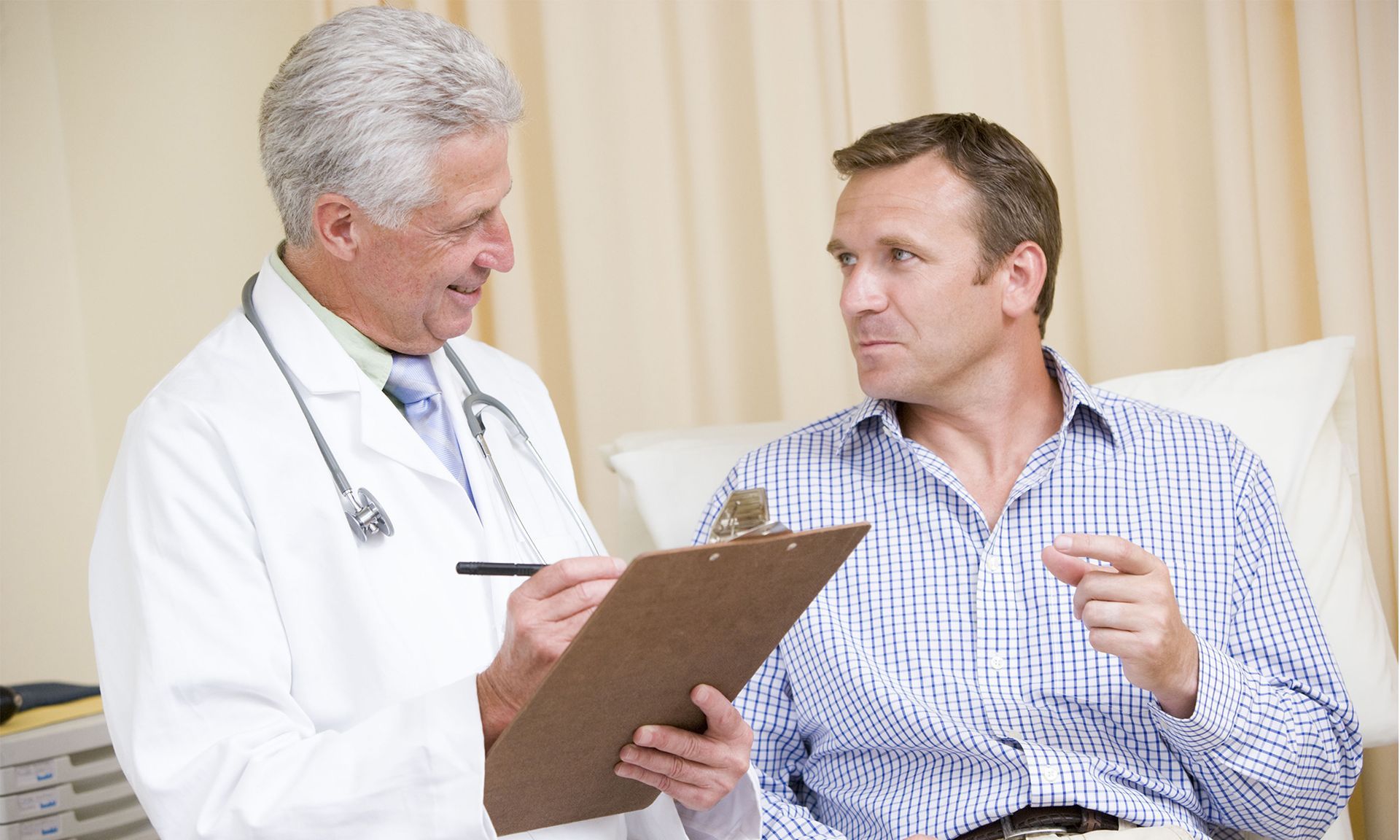 Doctor consulting with a patient in a hospital bed, holding a clipboard in a bright room