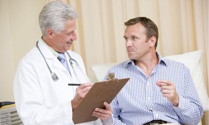 Doctor consulting with a patient in a hospital bed, holding a clipboard in a bright room