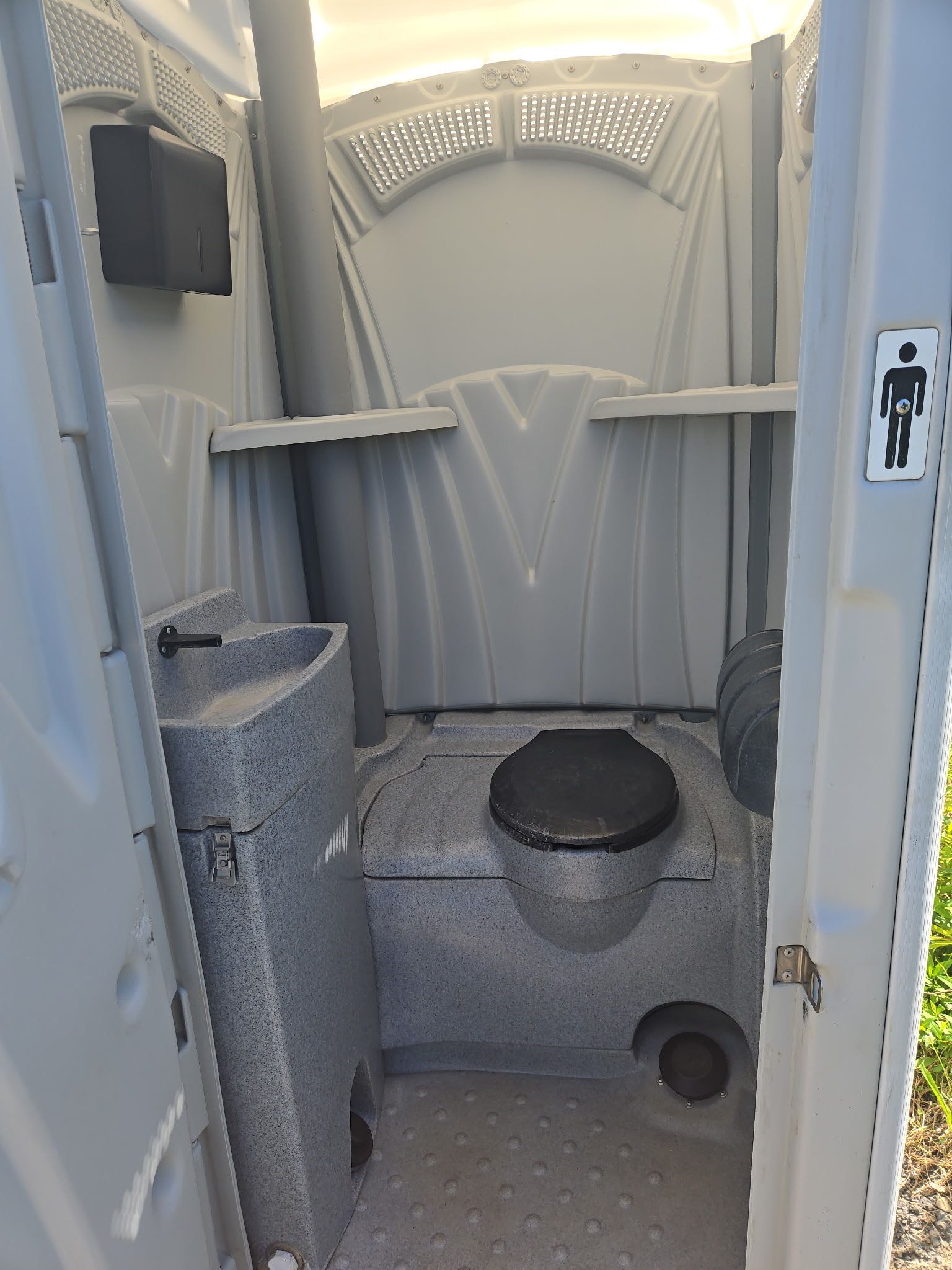 Interior view of a gray portable toilet with a sink, toilet, and shelf.