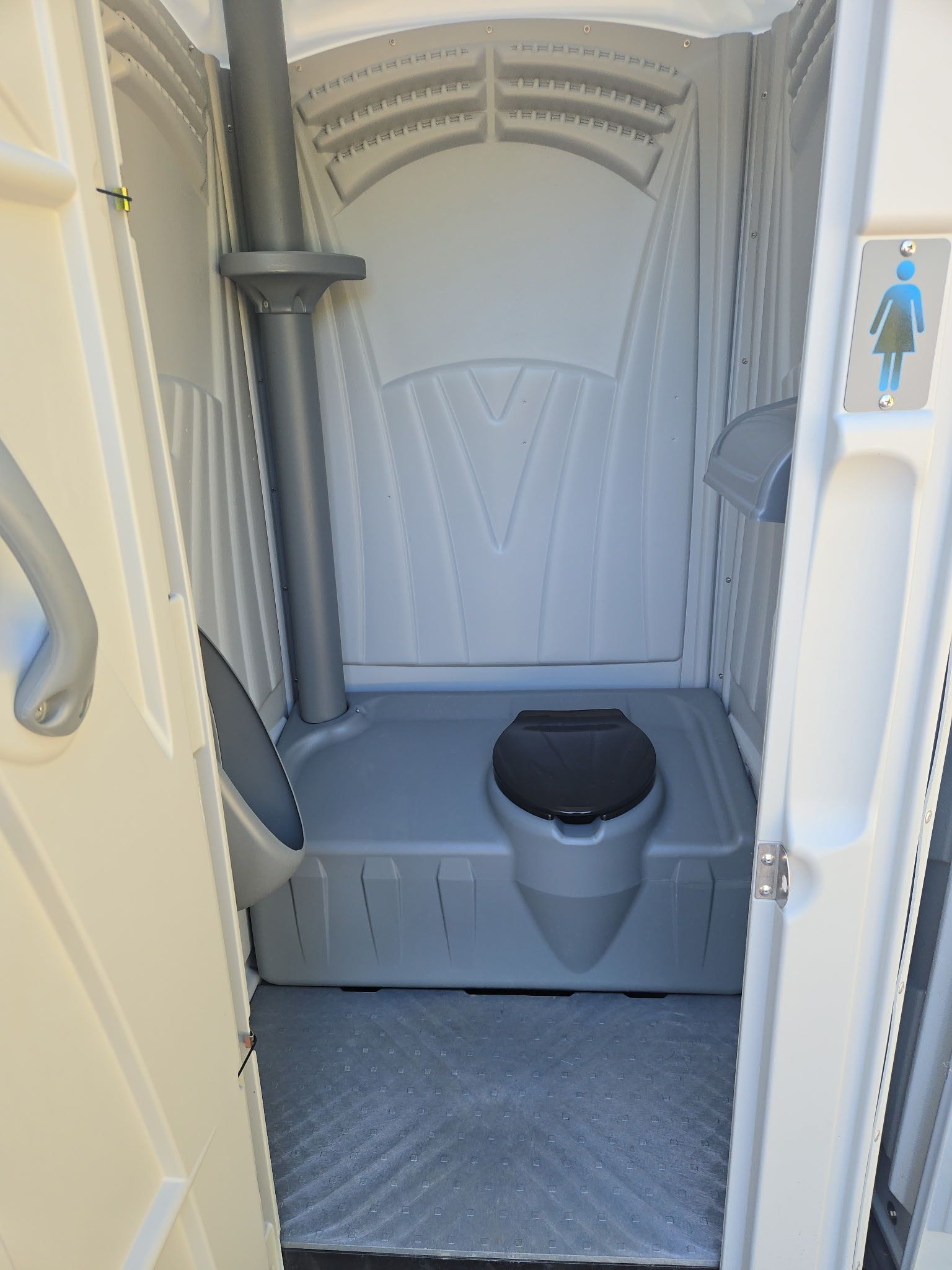 Interior of a portable toilet with gray walls, toilet seat, and a women's restroom symbol on the door.