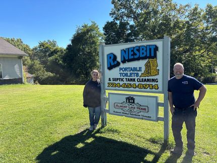 Two people standing beside a large Nesbit Pressure Washing & Window Cleaning sign in a sunny yard