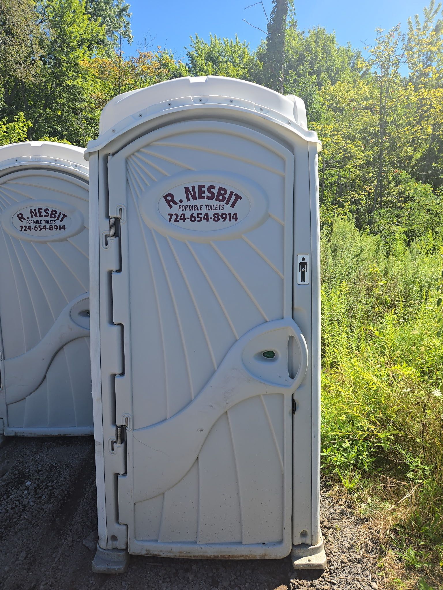 Two portable toilets on gravel. Grey plastic with company name, phone number, and lock visible.