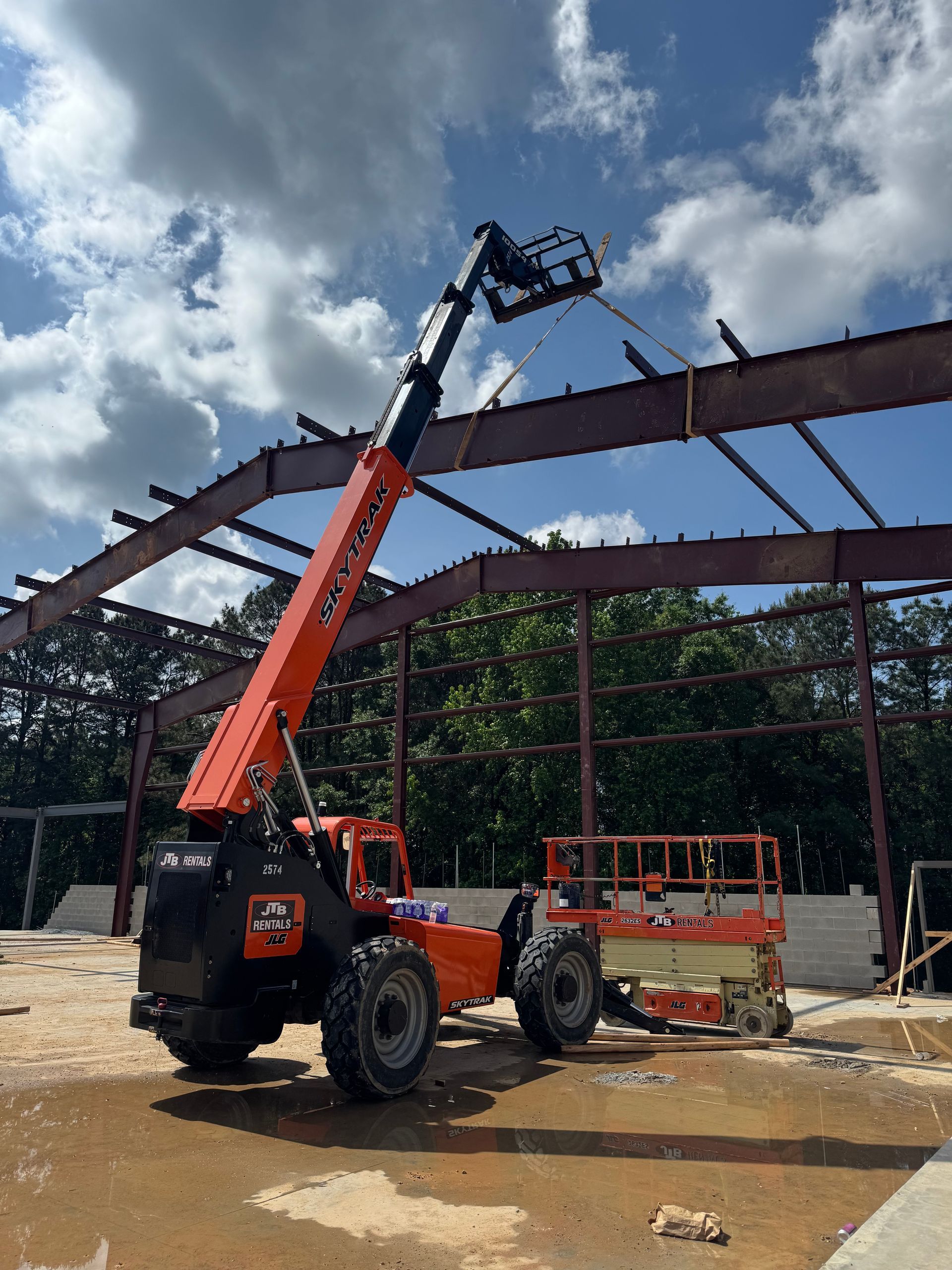 Orange telehandler lifting steel beams on a construction site.