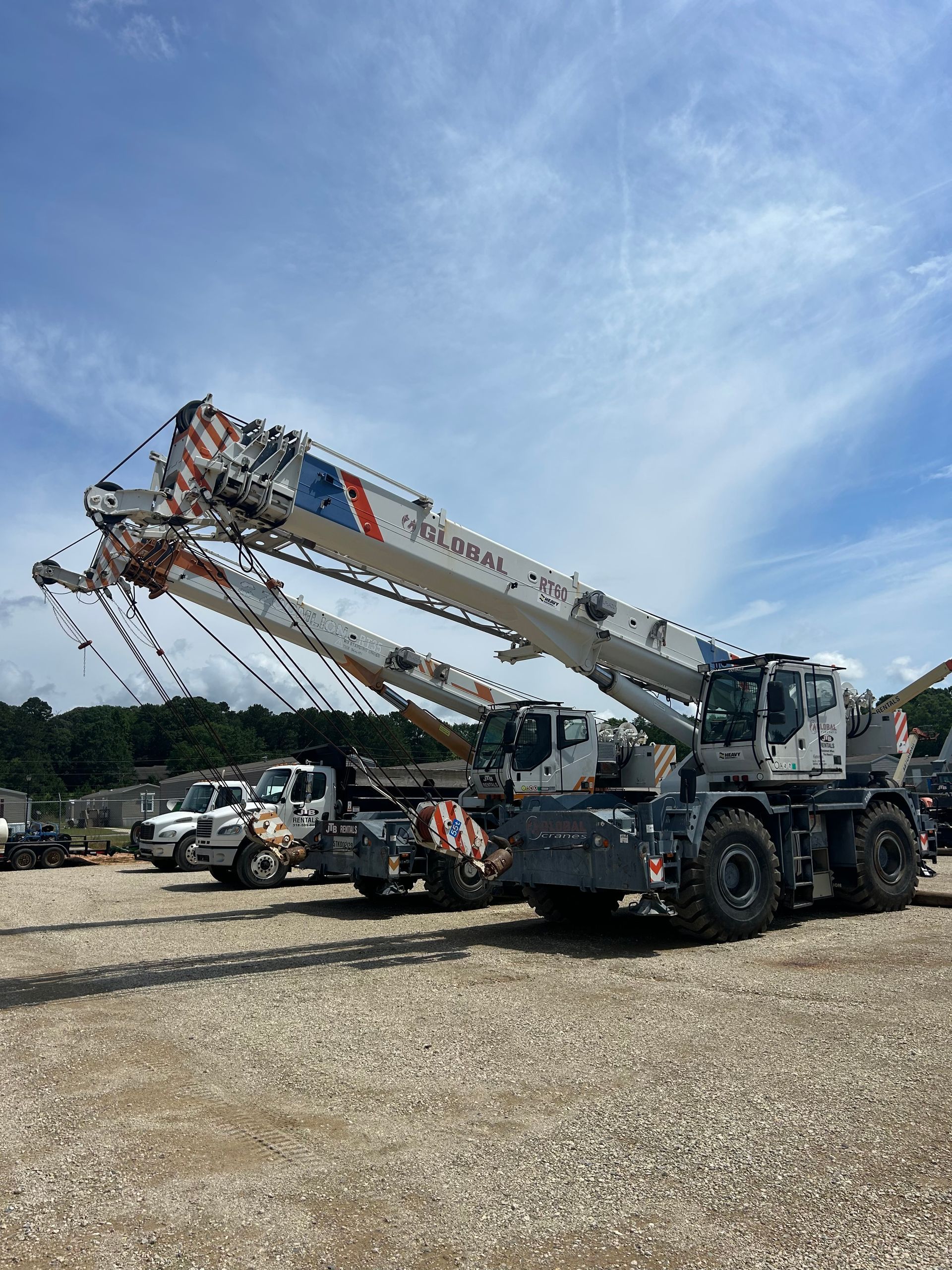 Three white and gray mobile cranes parked on gravel against a blue sky.