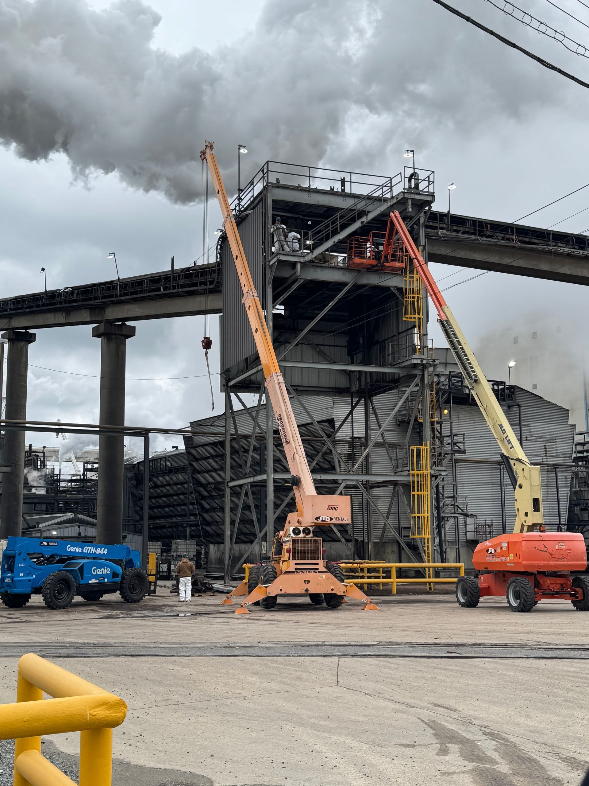 Industrial site with smokestacks, construction equipment, and a cloudy sky.
