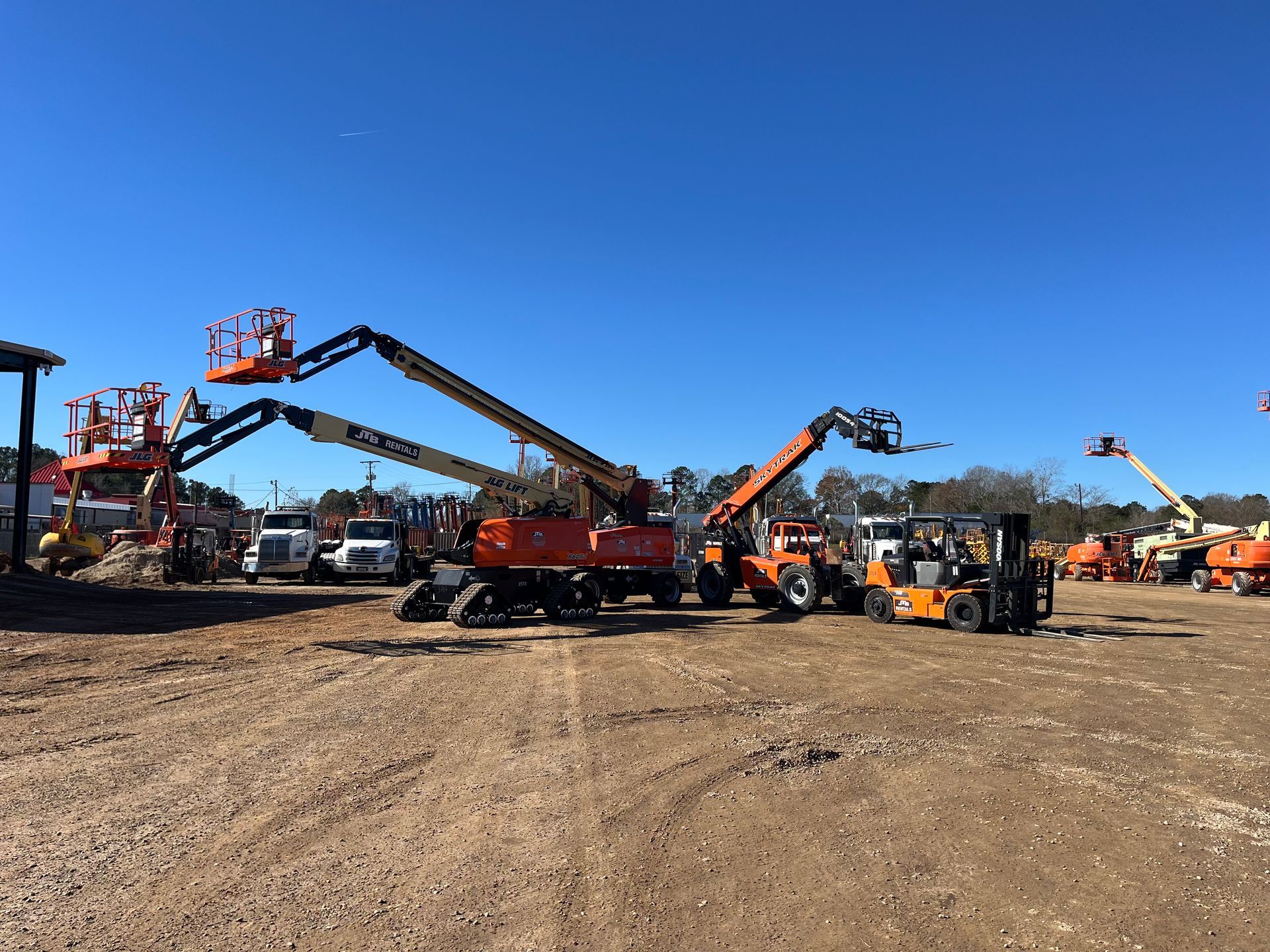 Construction equipment on a gravel lot under a clear blue sky. Various lifts and forklifts are present.