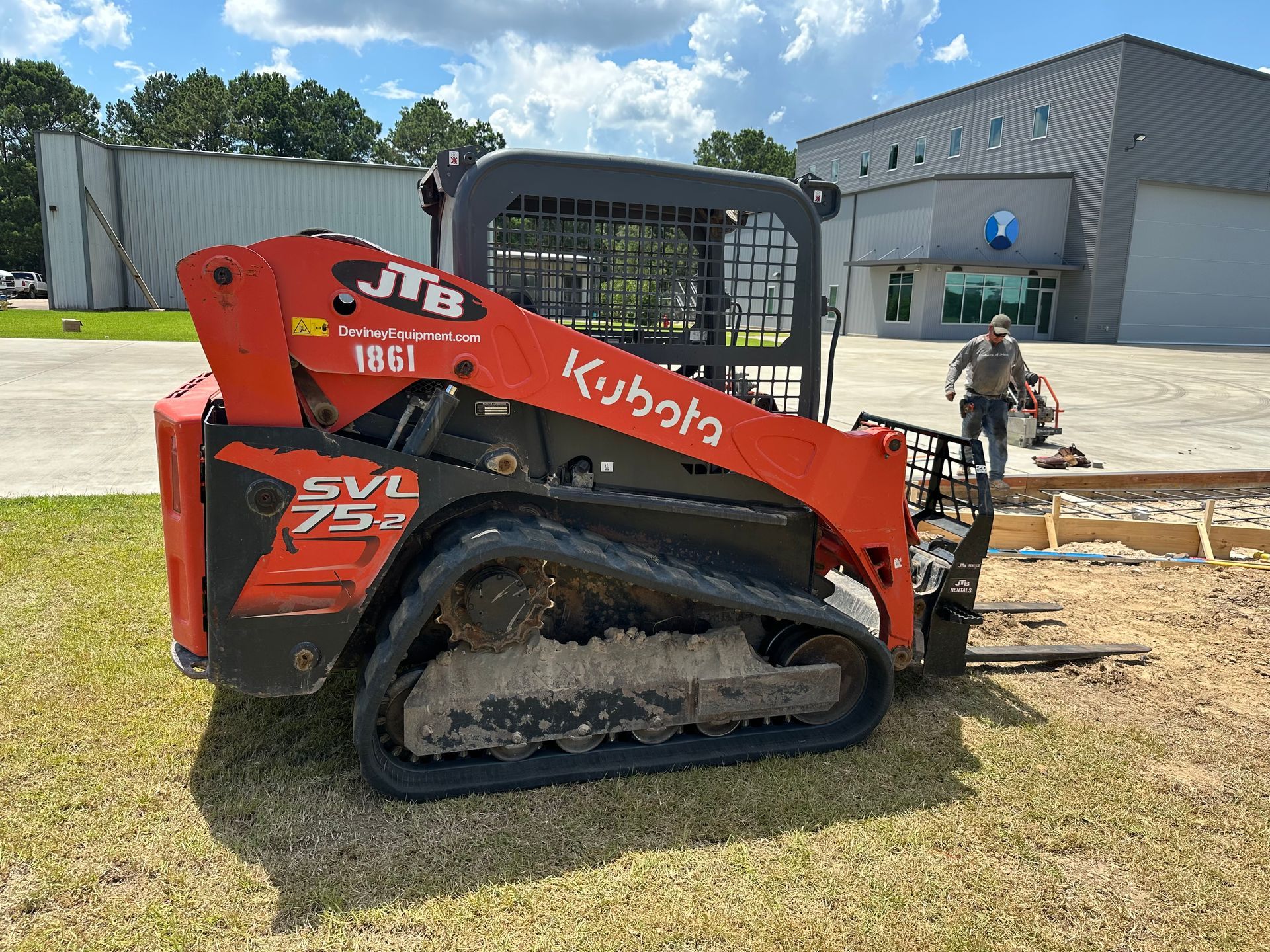 Orange Kubota track skid steer on grass, man near concrete form.