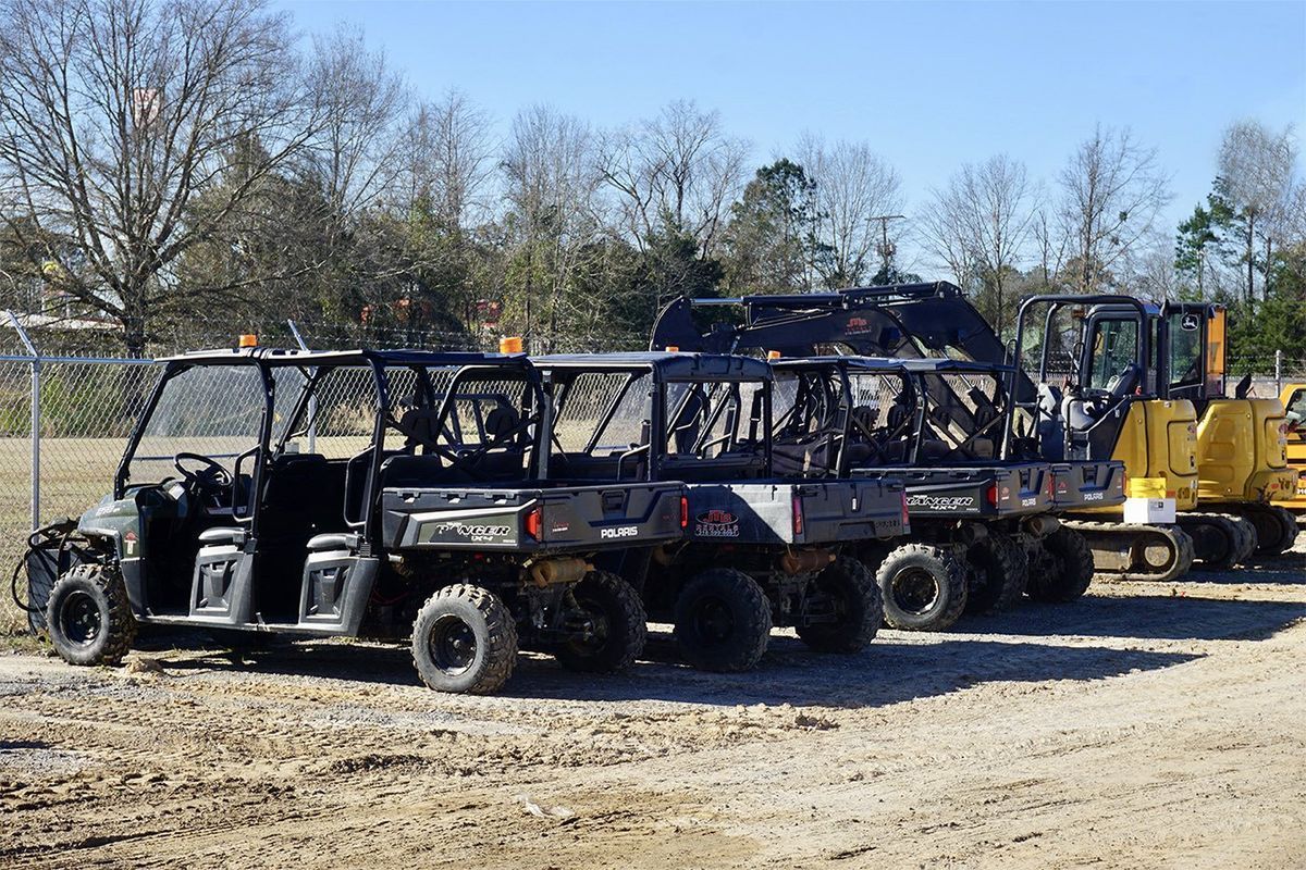 Four utility task vehicles parked on dirt, with construction equipment visible in the background.