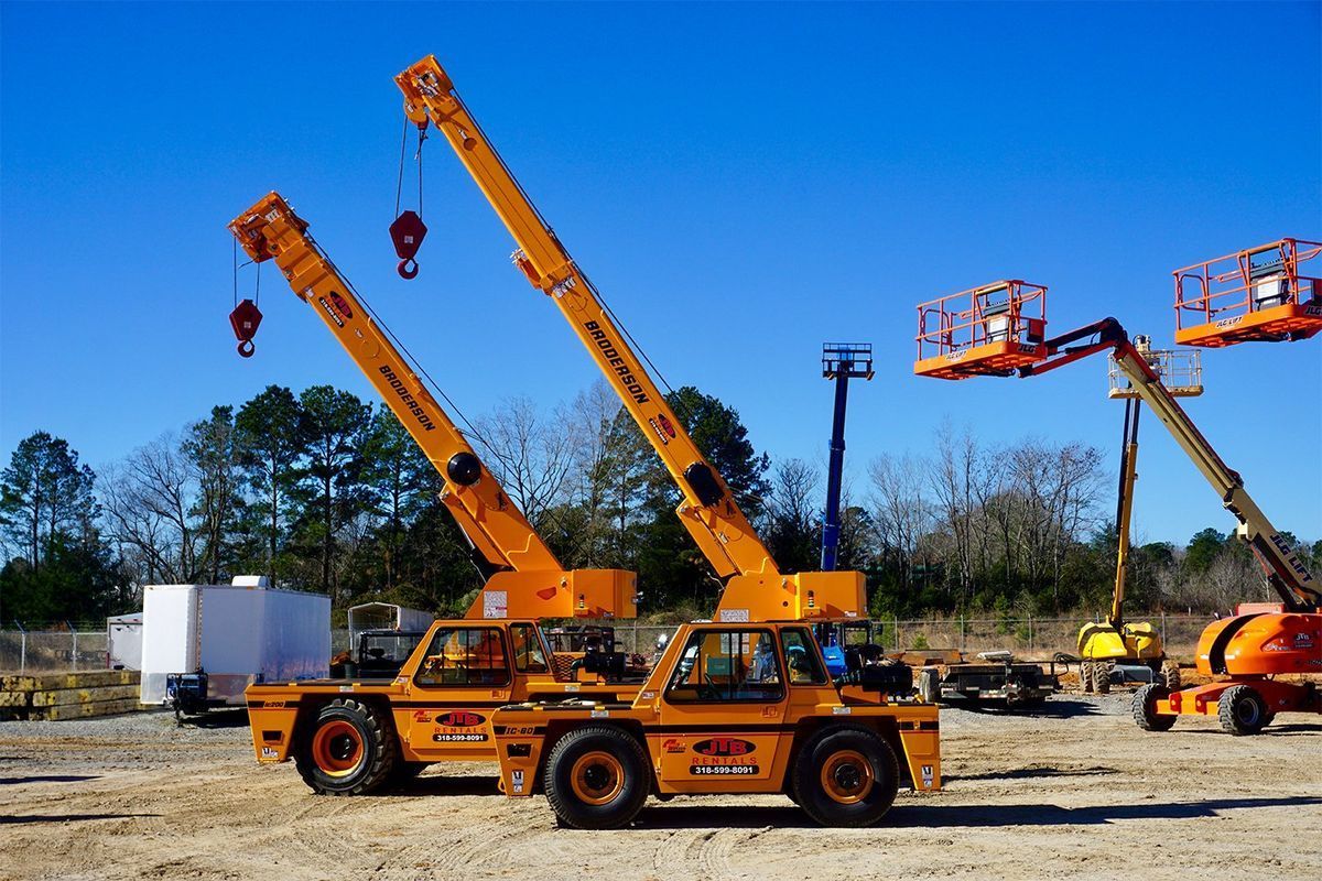 Two orange mobile cranes on a construction site with other equipment under a clear blue sky.