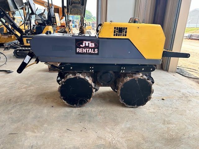 Yellow and gray JTB Rentals mini skid steer on a concrete surface with two axles and four wheels.