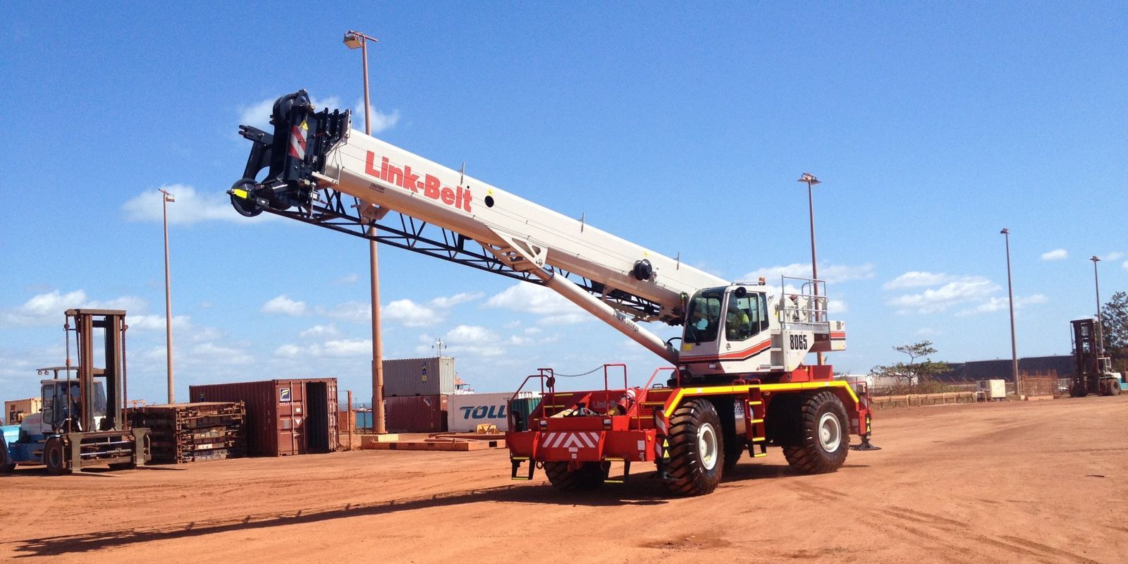A white and red Link-Belt crane on a red dirt surface with a blue sky.