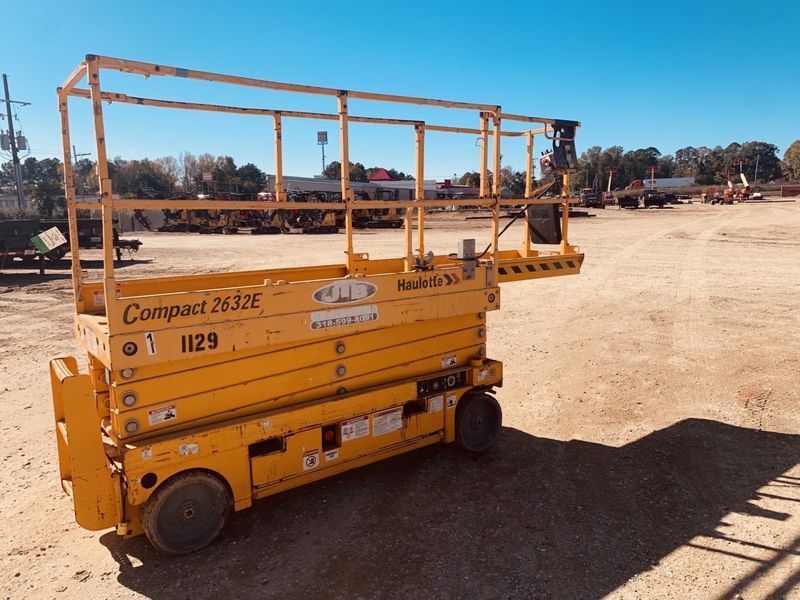 Yellow compact scissor lift on a dirt lot under a clear blue sky.
