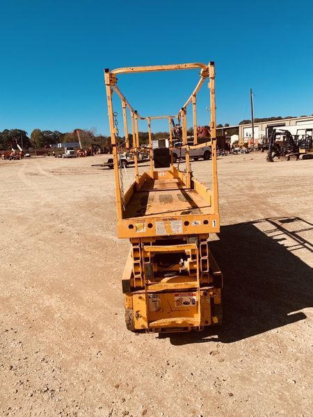 Yellow scissor lift on a dirt lot under a clear blue sky.