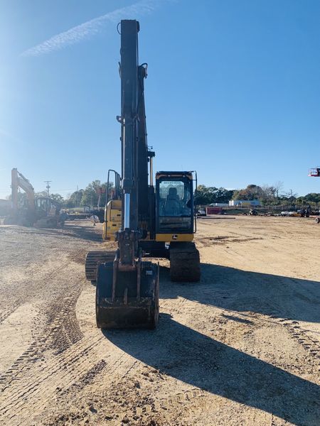 Yellow and black excavator on a dirt lot with a tall arm extended. Blue sky.
