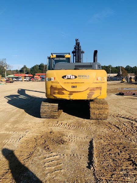 Yellow excavator on a construction site, viewed from the rear, tracks on the ground, sunny day.