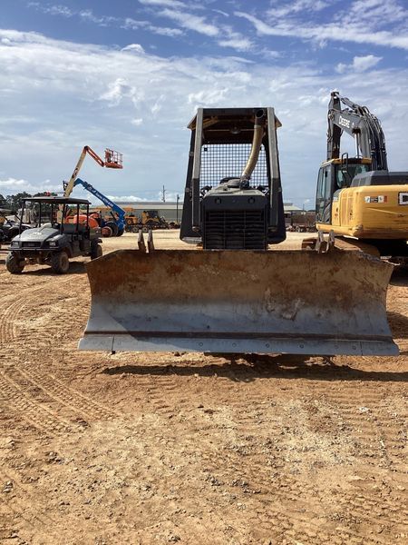 Bulldozer with blade in front, dirt lot setting. Other construction vehicles in background under cloudy sky.