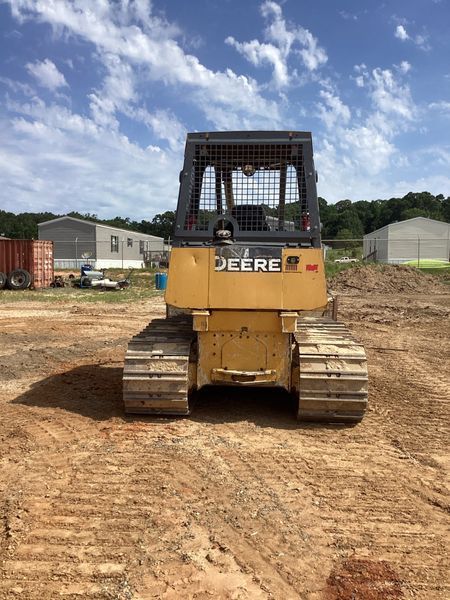 Yellow John Deere track loader on a dirt lot, against a blue sky with clouds.