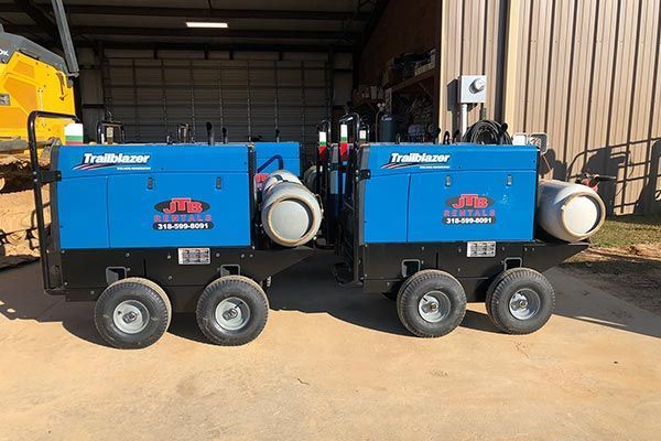 Two blue Miller Trailblazer welding machines on wheels, parked outdoors.
