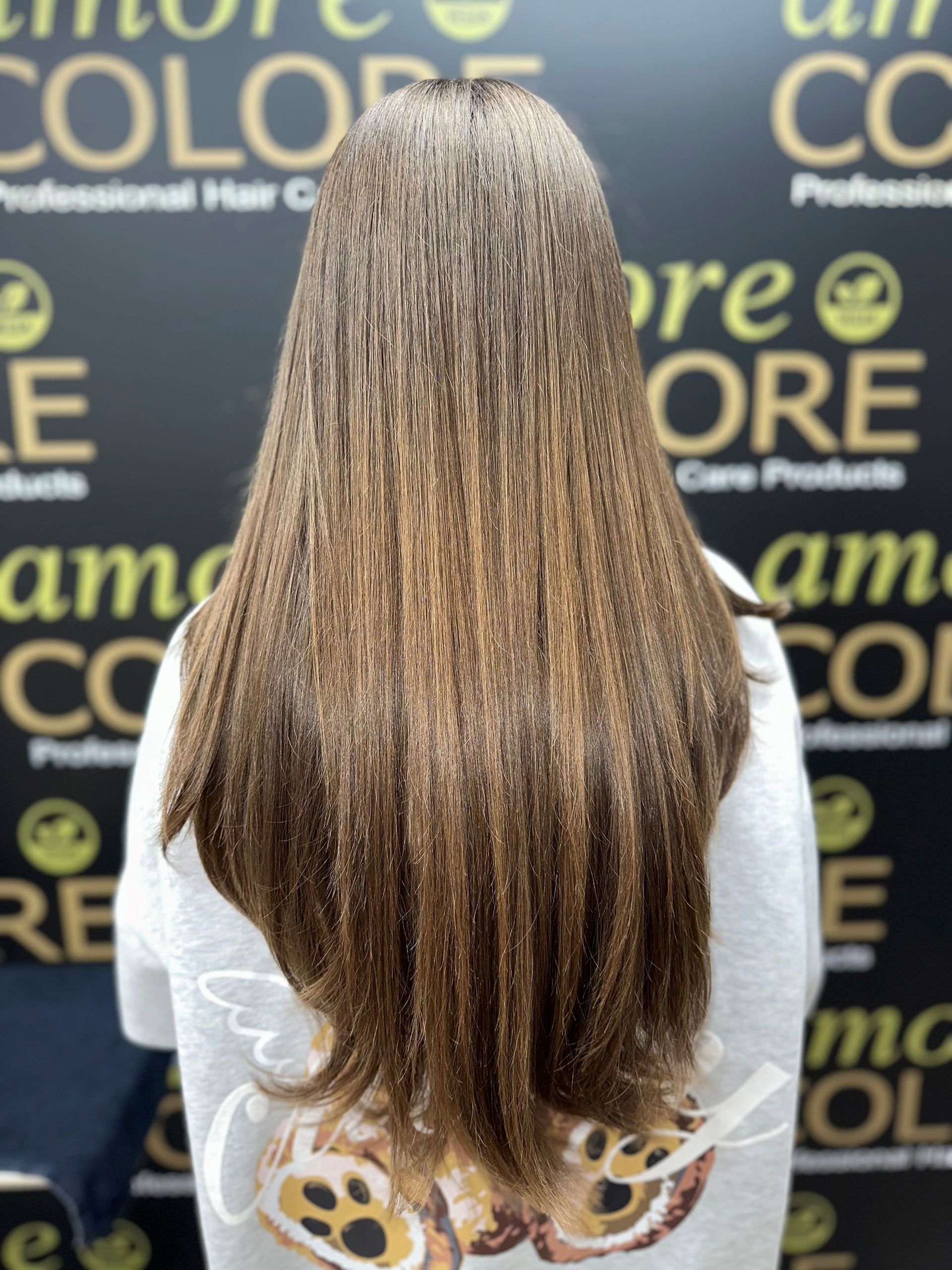 Woman with long, layered brown hair, standing in front of a black backdrop with text 