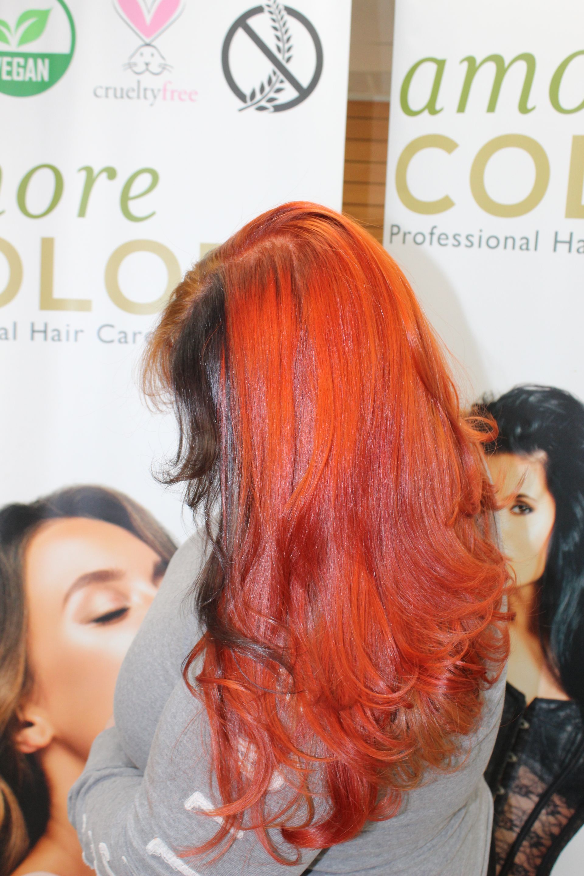 Woman with vibrant red hair, dark roots, stands in front of a hair care product display.