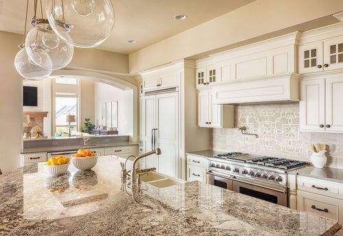 Bright white kitchen with marble island, stainless stove, and hanging glass pendant lights.