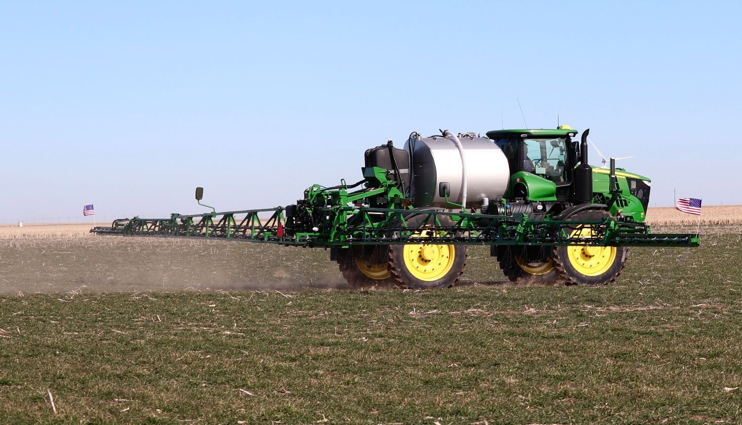 A green and yellow tractor is spraying a field