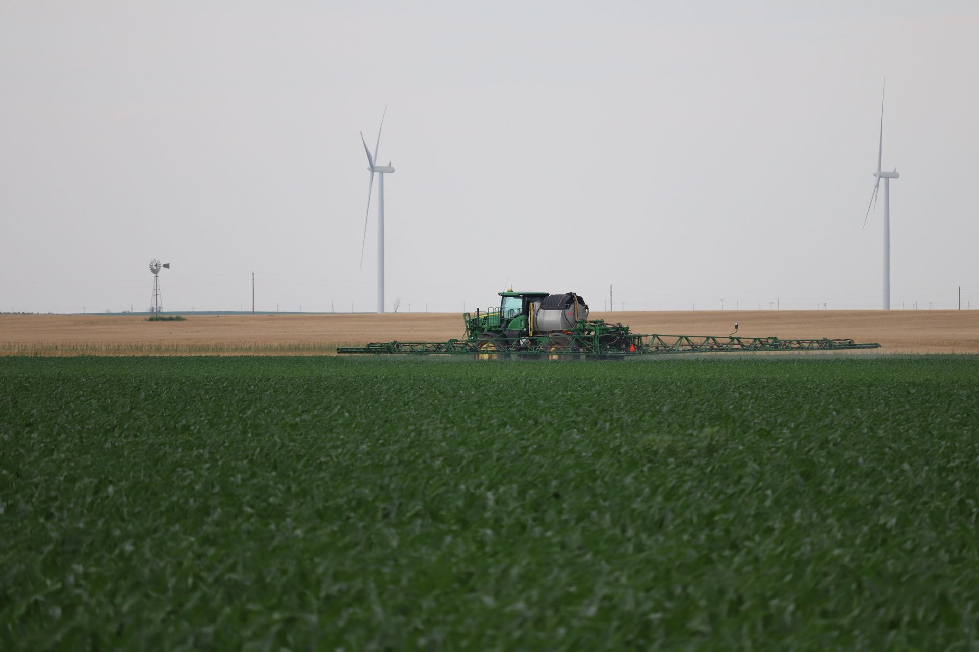 A tractor is spraying fertilizer on a field with windmills in the background.