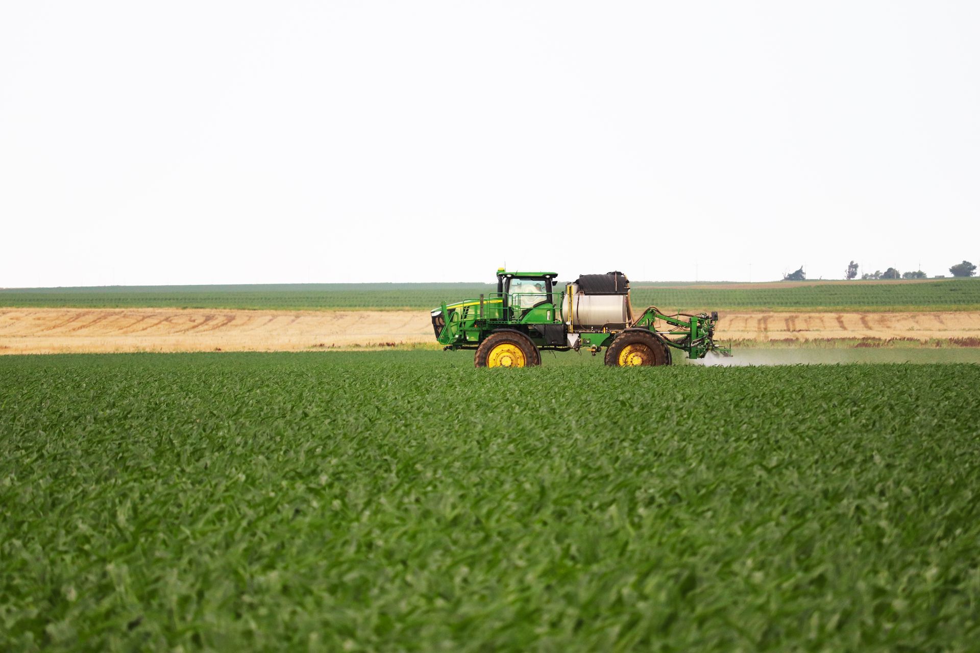 A green tractor is spraying fertilizer on a lush green field.