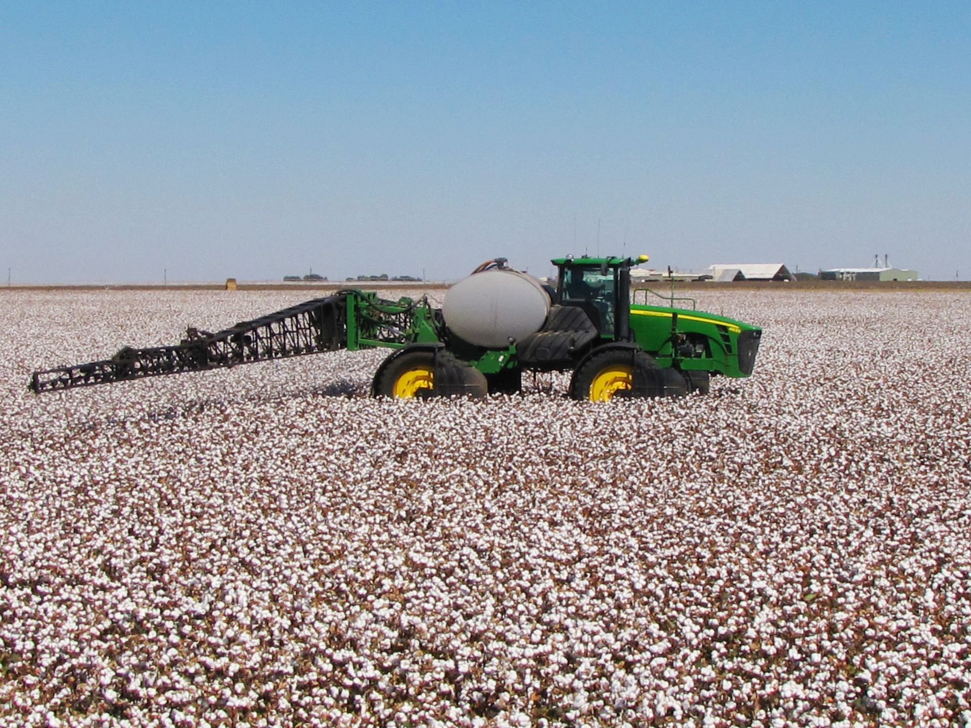 A john deere tractor is spraying cotton in a field
