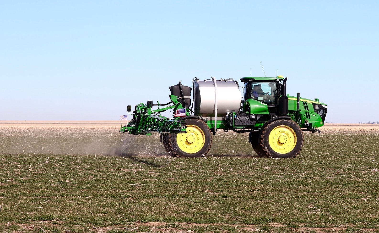 A green and yellow tractor is spraying a field.