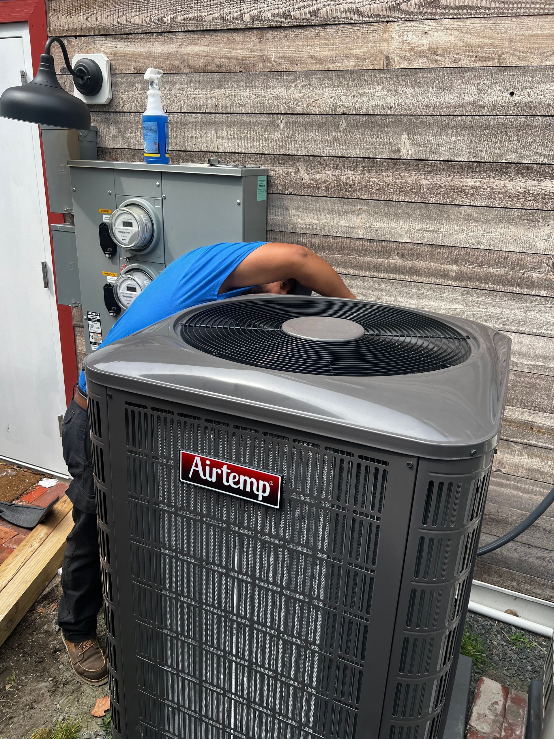 A man is working on an air conditioner outside of a building.