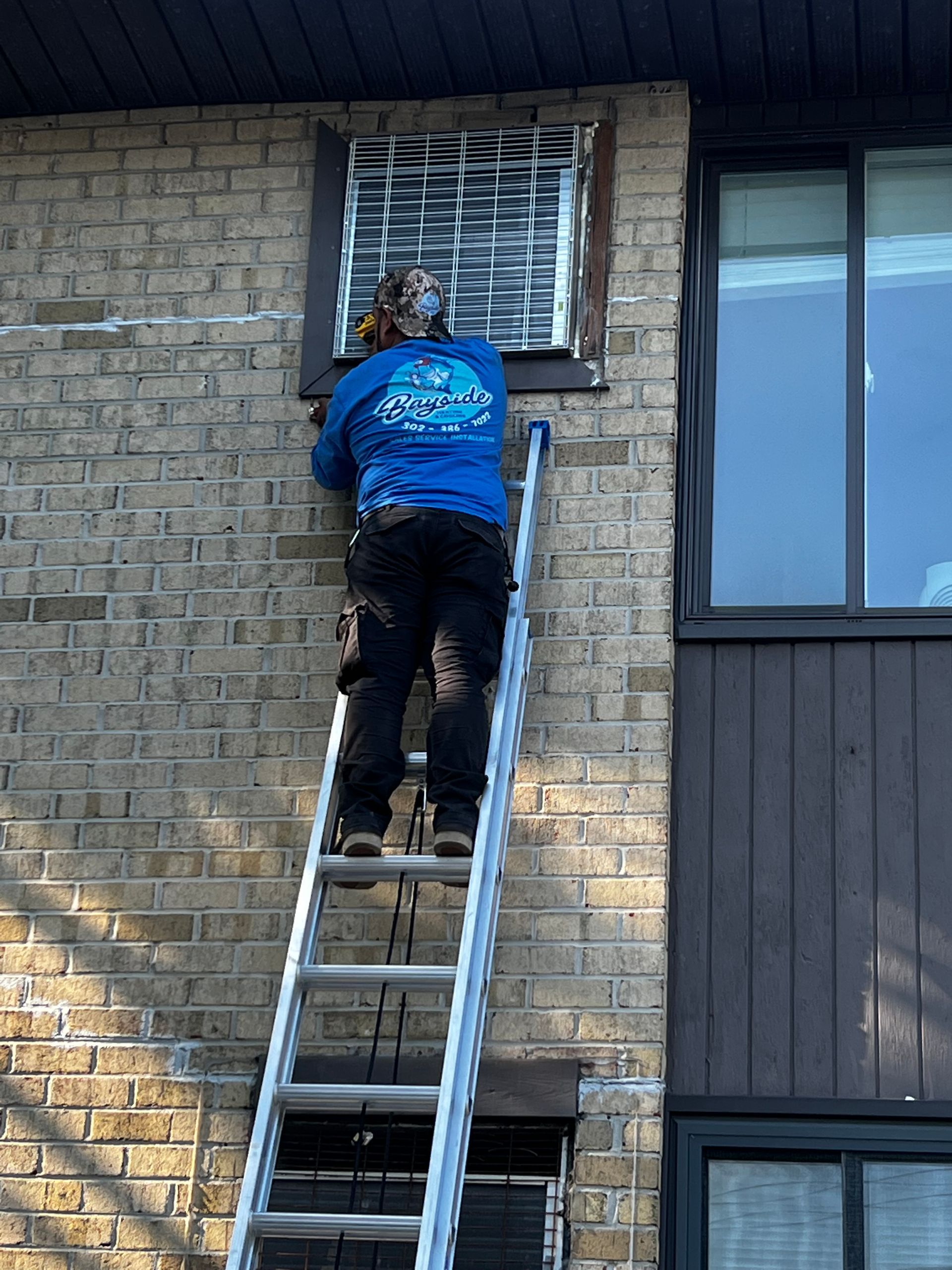 A man is climbing a ladder to fix a window on a brick building.