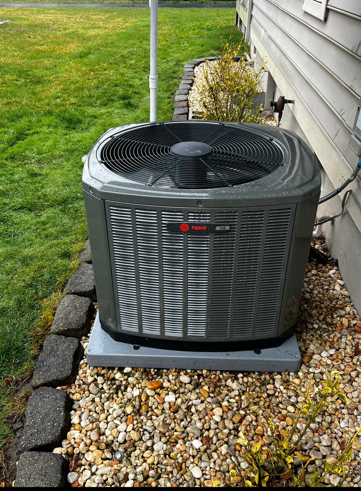 An air conditioner is sitting on top of a pile of gravel next to a house.