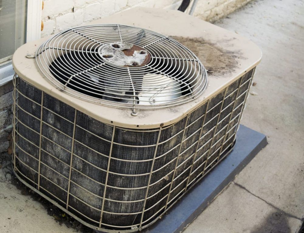 A dirty air conditioner is sitting on the sidewalk